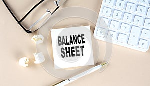 BALANCE SHEET text on sticky with pen ,calculator and glasses on beige background