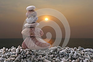 Balance stone on pile rock with sunset sea background.