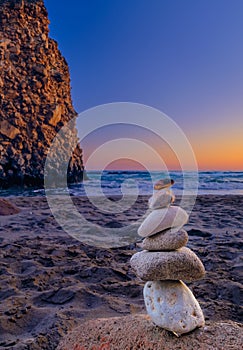 Balance stone stack and big natural rock on sandy beach at sunset.