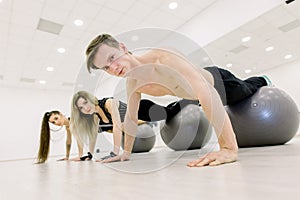 Balance, strength concept. Sporty man and two women do handstand with legs on fit ball. People in sportswear training on