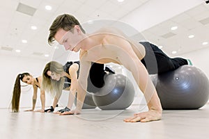 Balance, strength concept. Sporty man and two women do handstand with legs on fit ball. People in sportswear training on