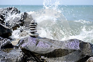 Balance zen stones pyramid on pebble beach with a splashing wave. Stability, balance, and harmony concept