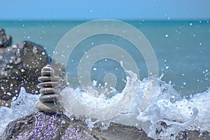 Balance zen stones pyramid on pebble beach with a splashing wave. Stability, balance, and harmony concept