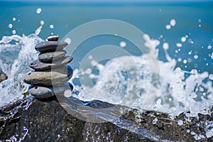 Balance zen stones pyramid on pebble beach with a splashing wave. Stability, balance, and harmony concept