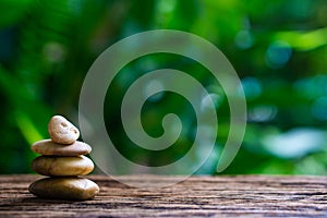 Balance Zen stones on wood with green nature bokeh background.