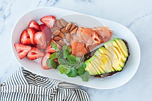 Balanced breakfast with avocado toast, salmon, nuts and fresh berries