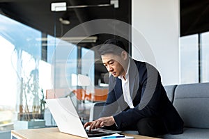 Balanced and calm businessman, asian man thinking working at laptop sitting in the office by the window