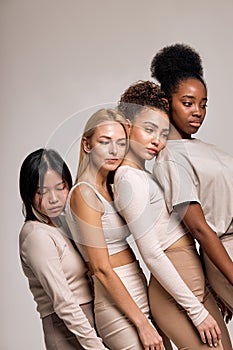 Balanced, calm diverse female models leaned on each other posing, looking down, isolated