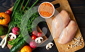 Balanced nutrition on a dark background, fresh vegetables and herbs on a cutting board and raw chicken, top view