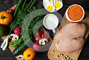 Balanced nutrition on a dark background, fresh vegetables and herbs on a cutting board and raw chicken, top view