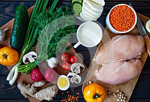 Balanced nutrition on a dark background, fresh vegetables and herbs on a cutting board and raw chicken, top view