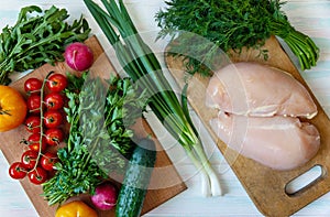 Balanced nutrition on a light background, fresh vegetables and herbs on a cutting board and raw chicken fillet, top view with