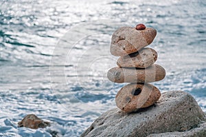 Balanced pebble pyramid on the beach on a sunny day. Sea foam on the background. Selective focus. Zen stones on the sea