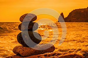 Balanced pebble pyramid on the beach on a sunset time. Sea waves and foam on the background. Selective focus. Zen stones on the