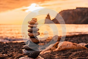 Balanced pebble pyramid on the beach on a sunset time. Sea waves and foam on the background. Selective focus. Zen stones