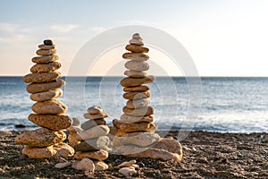 Balanced pebble pyramid silhouette on the beach. Abstract warm sunset bokeh with Sea on the background. Zen stones on
