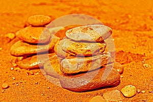 Balanced stacked stones or pebbles on black volcanic sand in orange