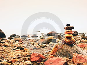 Balanced stone pyramid on sea shore, waves in background. Colorful flat stones