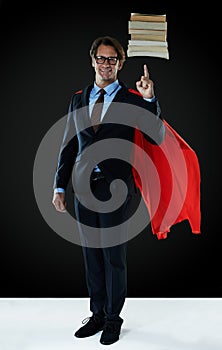 Balancing the books like a hero. Shot of a businessman wearing a red cape hovering books over his finger.