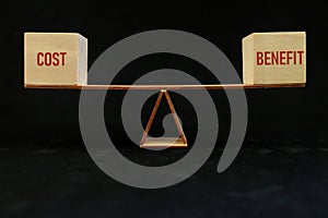Balancing cost and benefit word on seesaw scale in dark black background. Cost-benefit ratio business concept. photo