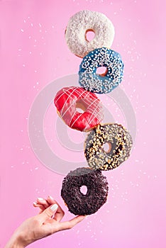 Balancing donuts on the tip of the woman`s finger. Multicolored decorated doughnuts in motion flying on pink background.