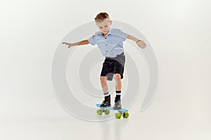 Balancing. Playful, active kid, boy riding on skateboard over grey studio background. Concept of game, childhood