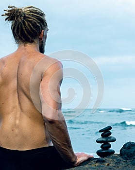 Balancing stones arranged in a pyramid shape with a back of a shirtless man meditating