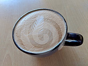 Balck cup of Cappuccino on saucer with a leaf pattern in foam photo