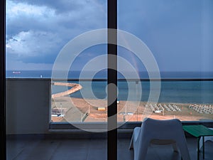 Balcony view of rainbow above the meditarranean sea, yachts and beach with sunbeds and volleyball court in Larnaca