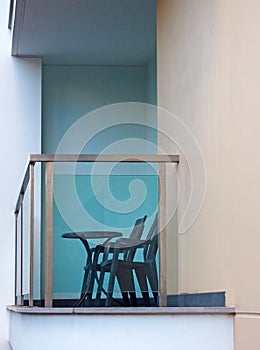 Balcony in a white modern concrete building with steel railings and a glass surround with black plastic chars and a table