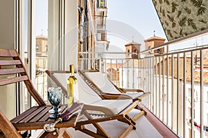 Balcony with wooden and fabric armchairs, a folding table of the same material and wine glasses with a bottle and a fabric awning