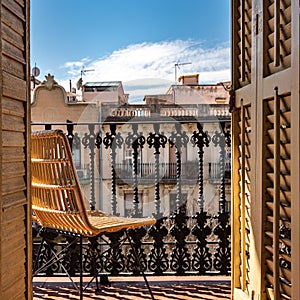 Balcony with a wrought iron railing, wooden sashes and wicker chair. Sunny day with blue sky. Barcelona, Spain. photo