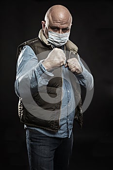 Bald adult man in a medical mask in a fighting stance. Unemployment and self-isolation during the coronavirus pandemic. Black