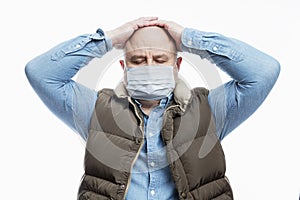 A bald adult man in a medical mask holds his head. White background. Close-up. Precautions during the coronavirus pandemic