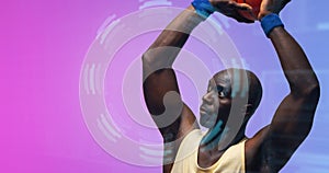 Bald african american basketball player with arms raised throwing ball by floral pattern, copy space photo