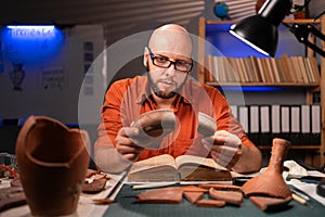Bald archaeologist working at night in the office studying ancient artifacts.
