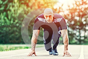 Bald Athletic Man in Running Start Position and Looking Into the Distance in stadium.