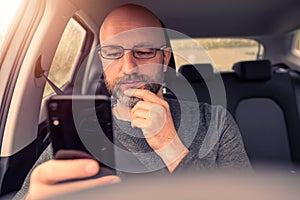 Bald attractive male driver in a car. The model in his 40s, wearing grey shirt. Grey and dark beard, metal glasses. Selective