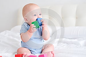 bald baby boy 3 months in blue bodysuit playing with children wooden cubes toys on bed