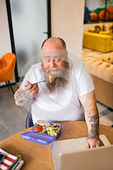 Bald bearded abdominous man in white tshirt having lhis meal