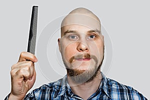 Bald bearded man with beard and comb in his hand combs against an isolated background