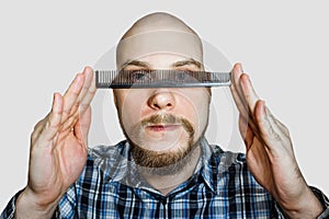 Bald bearded man with beard and comb in his hand combs against an isolated background