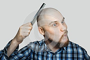 Bald bearded man with beard and comb in his hand combs against an isolated background