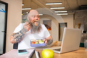 Bald bearded man in white tshirt having lunch sitting at the table