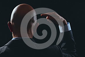 Bald business man in dark classic suit making hand gesture. Black background. Hands pointing to his head. Use your brain and think