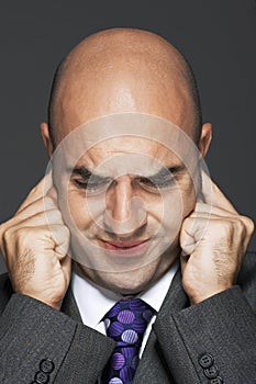 Bald businessman with fingers in ears making a face