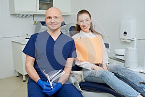 Bald dentist and a female patient with a smile are posing in a dentist`s office