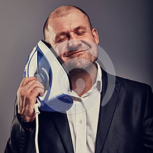 Bald fun happy comic business man holding the home iron near the face with love in suit on grey background. Closeup portrait.