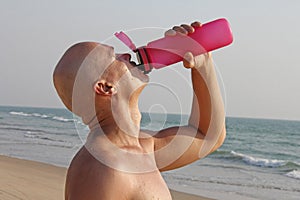 A bald, handsome man with a bare or bare torso is drinking water