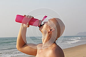 A bald, handsome man with a bare or bare torso is drinking water